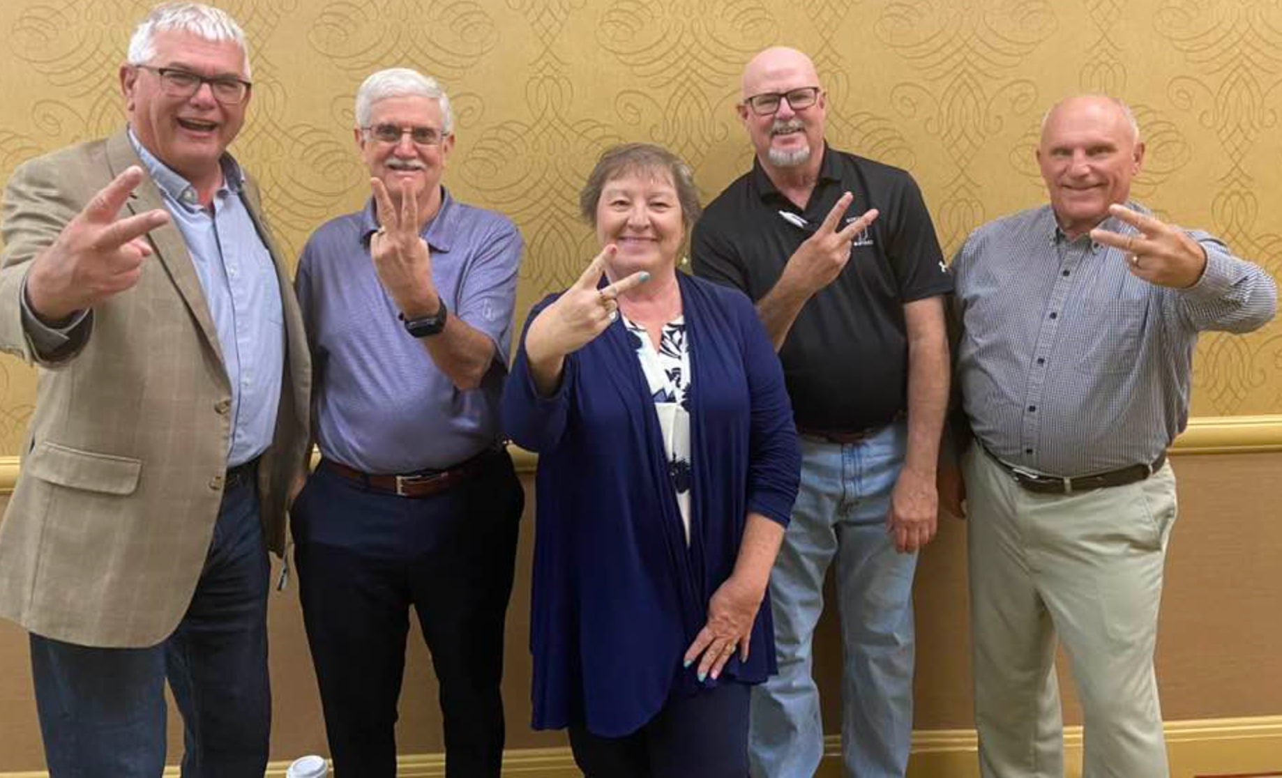 Denny Spinner, Harold “Huck” Lewis, Cathy Gross, Mark Senter, and Terry Seitz (pictured L-R) smiling for camera and holding their fingers in a V.